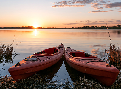 A photo of two kayaks landed on a sandy shore with tail grasses to the left and right with the sun on the horizon with a distance shoreline